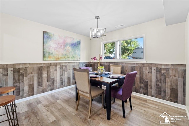 dining space featuring light hardwood / wood-style floors, a notable chandelier, and wood walls