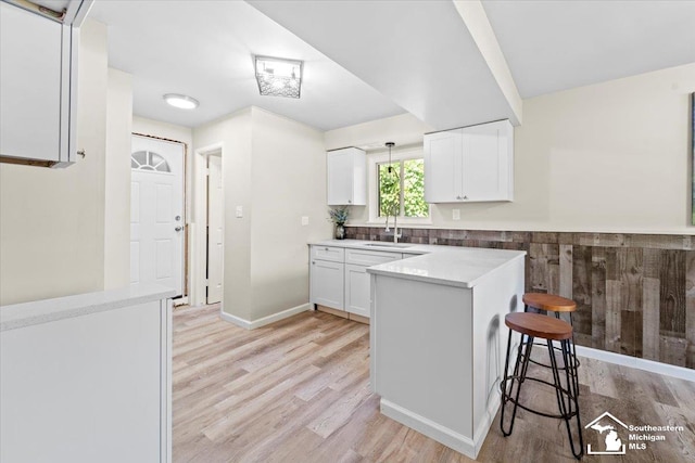 kitchen featuring kitchen peninsula, light wood-type flooring, sink, white cabinets, and a breakfast bar area