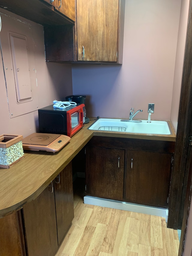 kitchen with dark brown cabinets, light hardwood / wood-style flooring, and sink