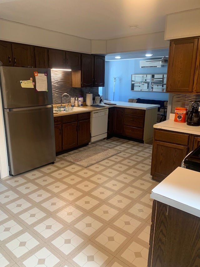 kitchen with stove, backsplash, white dishwasher, sink, and stainless steel refrigerator