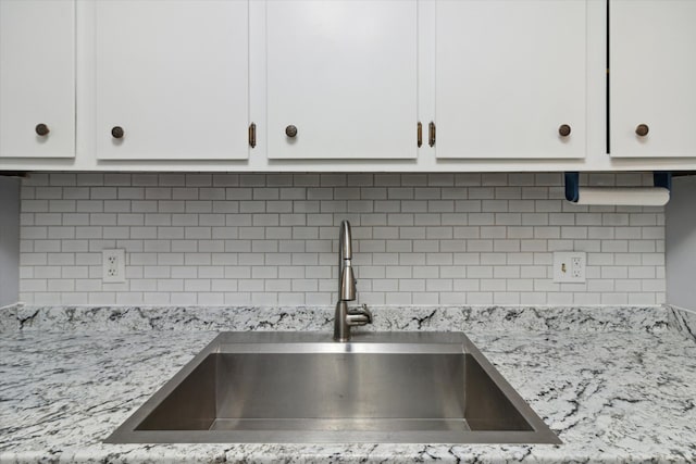 room details featuring backsplash, light stone countertops, white cabinetry, and sink