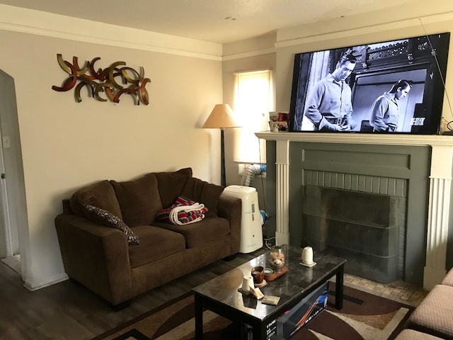 living room featuring ornamental molding, dark wood-type flooring, and a brick fireplace