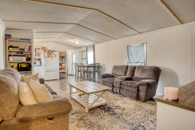 living room featuring a textured ceiling, light hardwood / wood-style flooring, and vaulted ceiling