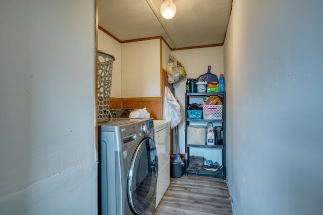 clothes washing area with a textured ceiling, hardwood / wood-style flooring, ornamental molding, and washing machine and clothes dryer