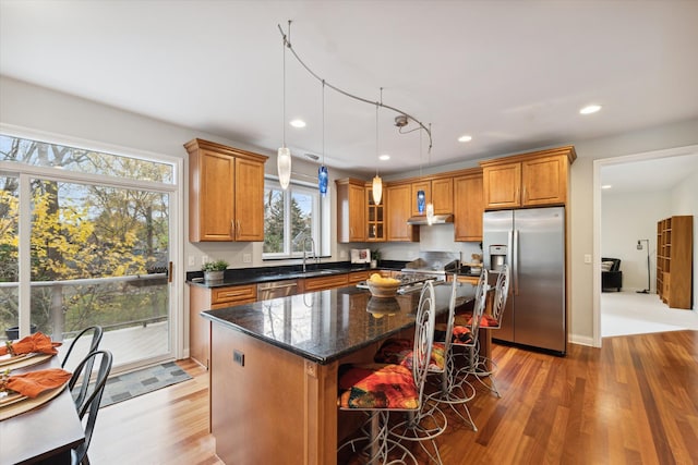 kitchen with appliances with stainless steel finishes, wood-type flooring, decorative light fixtures, dark stone countertops, and a kitchen island