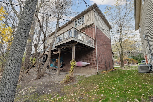 back of house featuring central air condition unit, a balcony, and a yard