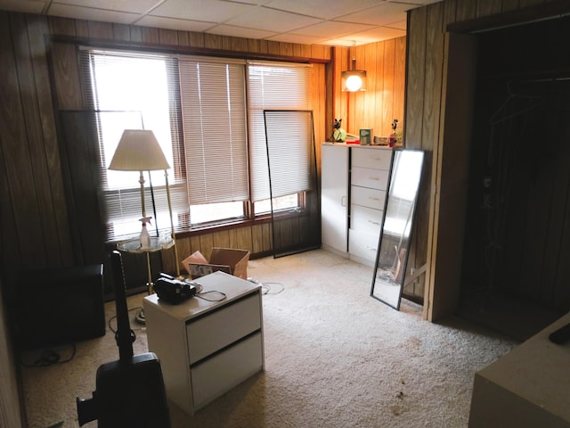 sitting room featuring light carpet, a drop ceiling, and wood walls