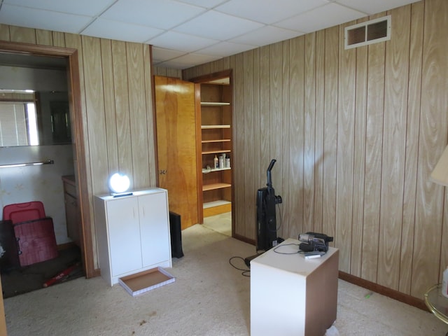 carpeted office space with a drop ceiling and wood walls