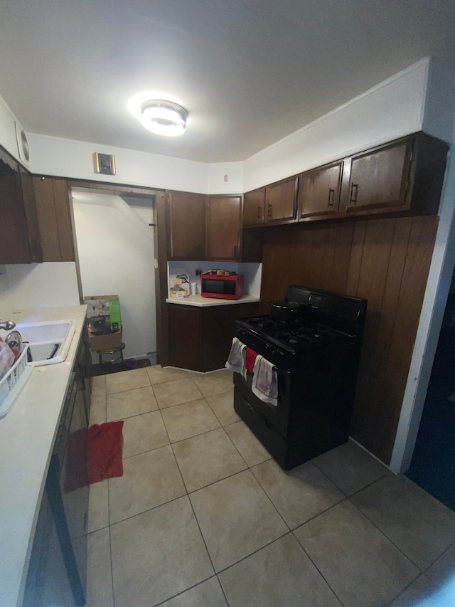 kitchen featuring dark brown cabinetry, sink, black range with gas cooktop, wooden walls, and light tile patterned floors