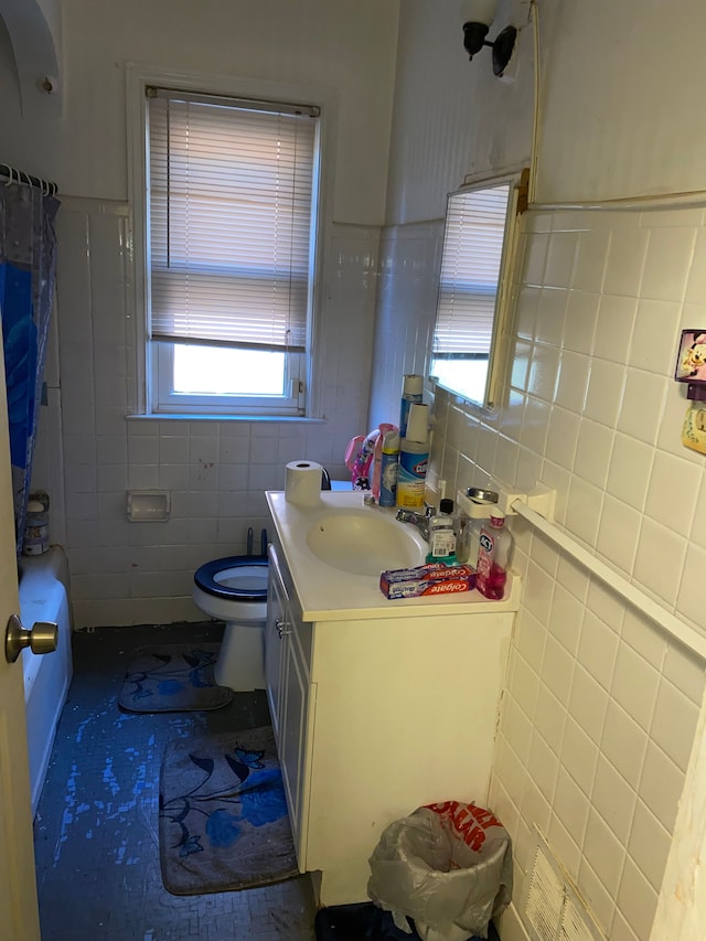 bathroom with vanity, a healthy amount of sunlight, toilet, and tile walls