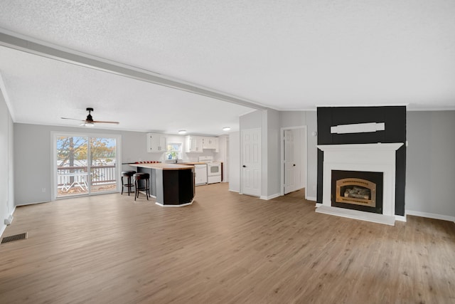 unfurnished living room with a fireplace, a textured ceiling, light wood-type flooring, and ceiling fan