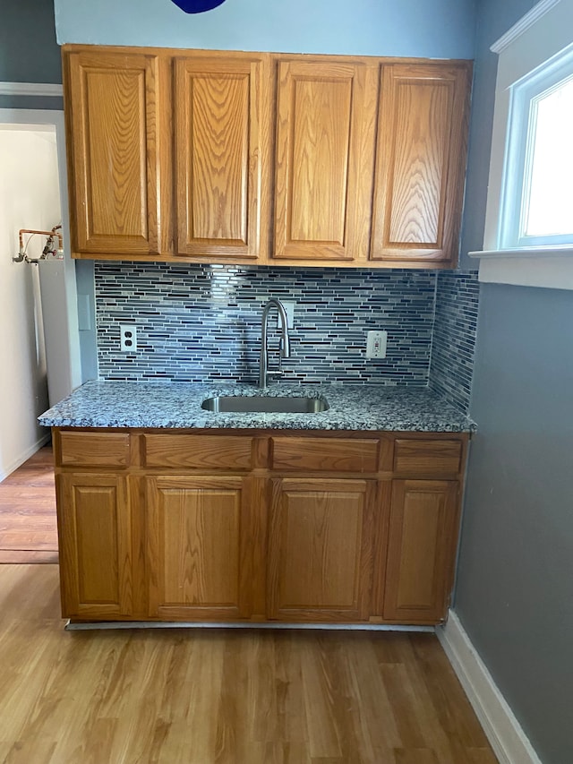 kitchen with decorative backsplash, light stone countertops, sink, and light wood-type flooring