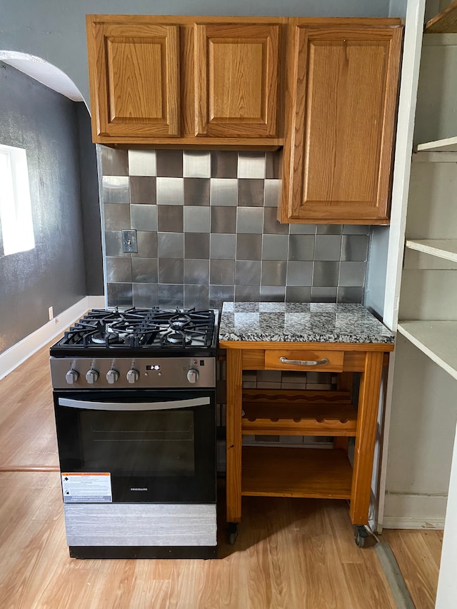 kitchen with light stone counters, stainless steel range with gas cooktop, light wood-type flooring, and tasteful backsplash