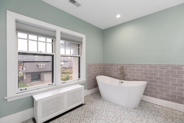 bathroom featuring a tub, radiator heating unit, tile walls, and tile patterned flooring