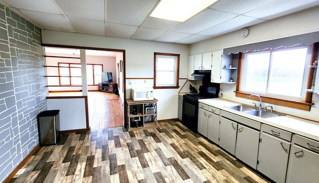 kitchen with a wealth of natural light, a drop ceiling, black range oven, and dark hardwood / wood-style floors