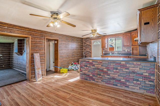 kitchen with kitchen peninsula, light hardwood / wood-style flooring, ceiling fan, and wooden walls