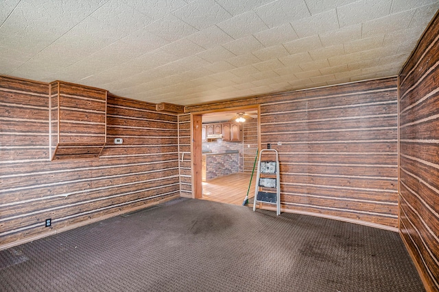 empty room with carpet flooring, wood walls, and ceiling fan