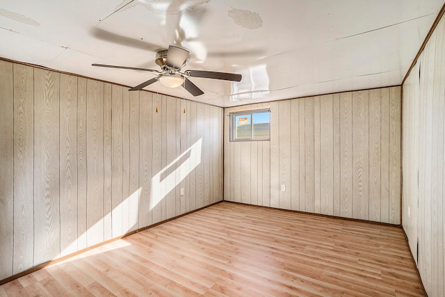 spare room featuring light hardwood / wood-style flooring, ceiling fan, and wooden walls