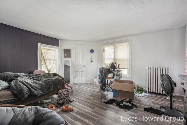 bedroom featuring wooden walls, dark wood-type flooring, radiator, and multiple windows