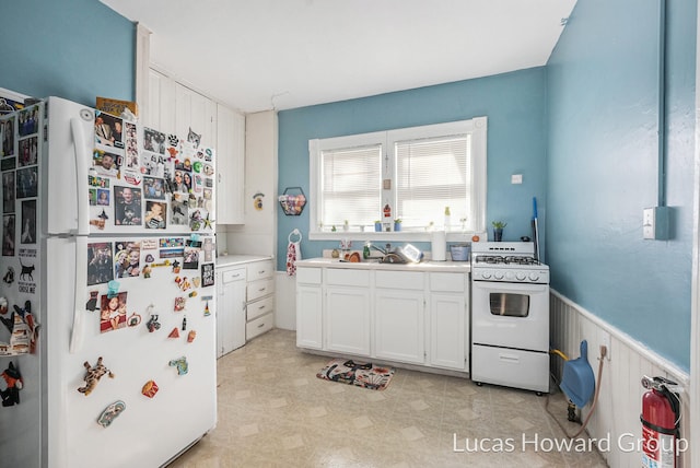 kitchen featuring wooden walls, sink, white cabinets, and white appliances