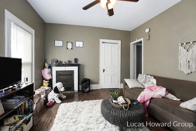 living room featuring dark hardwood / wood-style flooring, a stone fireplace, and ceiling fan