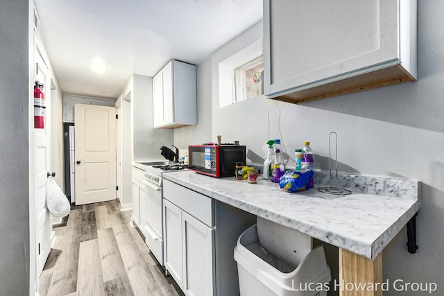 kitchen featuring white cabinets, light wood-type flooring, light stone counters, and white gas range