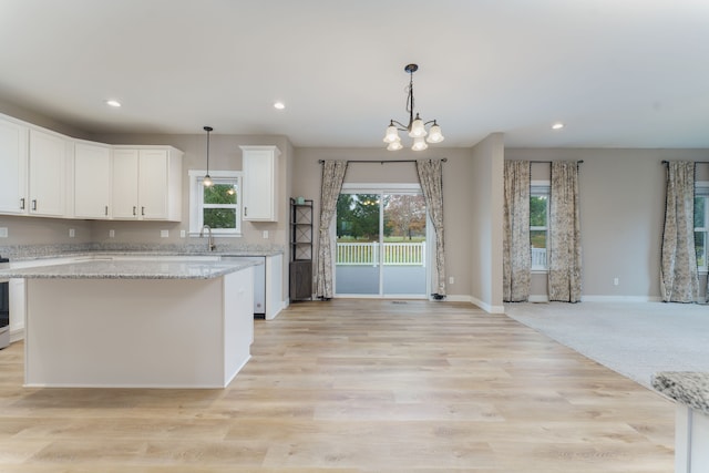 kitchen featuring white cabinets, light stone counters, light wood-type flooring, and hanging light fixtures