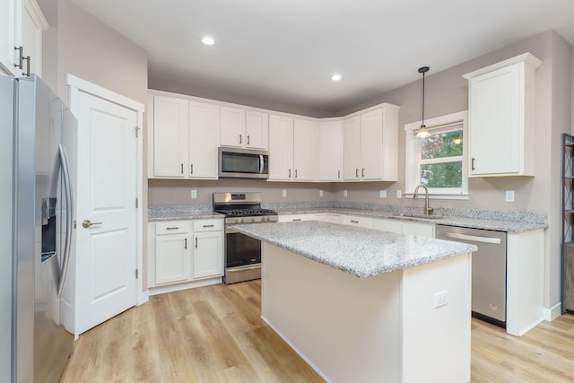 kitchen with appliances with stainless steel finishes, light wood-type flooring, a kitchen island, decorative light fixtures, and white cabinetry