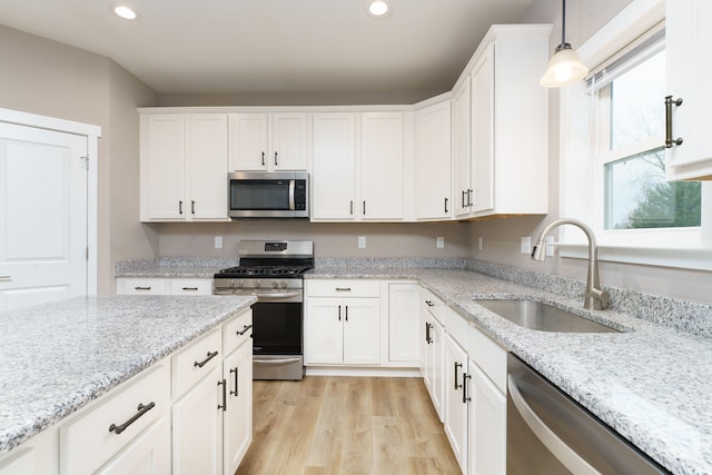 kitchen featuring white cabinets, sink, hanging light fixtures, light stone counters, and stainless steel appliances