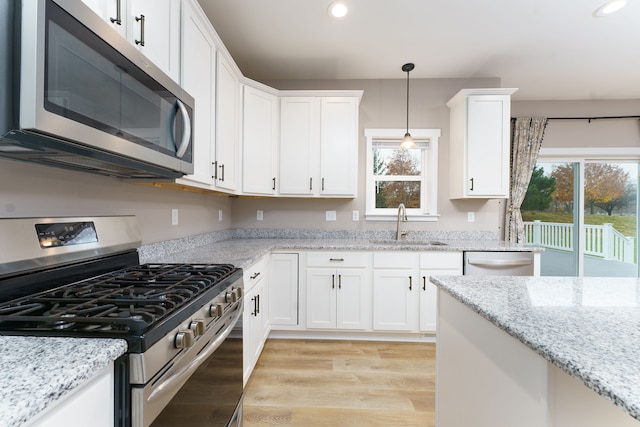 kitchen with white cabinetry, sink, stainless steel appliances, pendant lighting, and light wood-type flooring