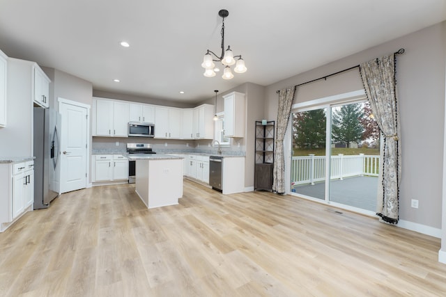 kitchen featuring a center island, white cabinets, appliances with stainless steel finishes, light hardwood / wood-style floors, and light stone counters