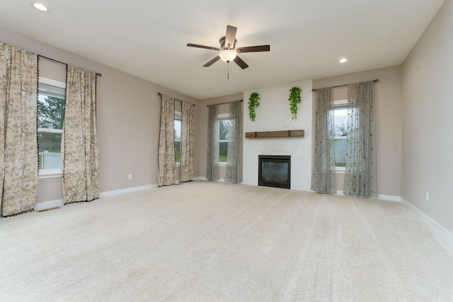 unfurnished living room featuring light carpet, a large fireplace, and ceiling fan