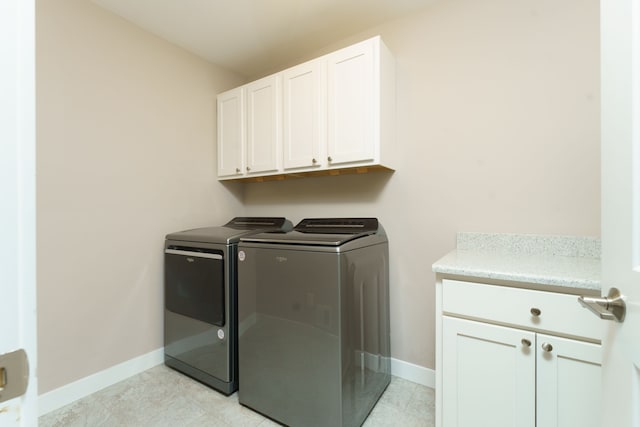 laundry area featuring washing machine and clothes dryer, light tile patterned floors, and cabinets