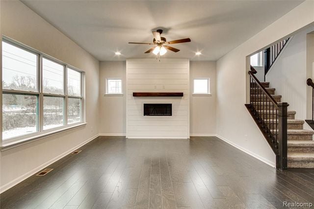 unfurnished living room with a large fireplace, ceiling fan, and dark hardwood / wood-style floors