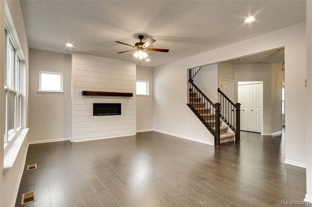 unfurnished living room featuring a large fireplace, ceiling fan, and dark wood-type flooring