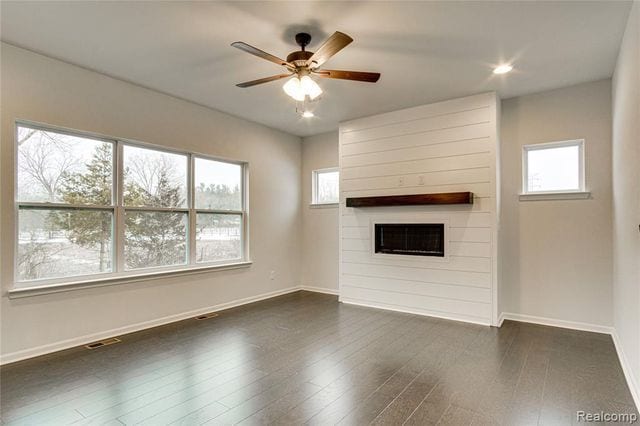 unfurnished living room with ceiling fan, a large fireplace, and dark hardwood / wood-style flooring