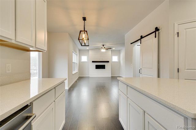 kitchen with a fireplace, dark wood-type flooring, a barn door, white cabinets, and hanging light fixtures