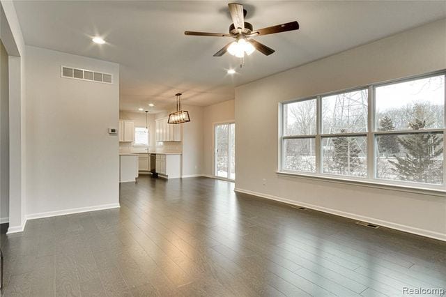 unfurnished living room featuring ceiling fan with notable chandelier and dark hardwood / wood-style flooring