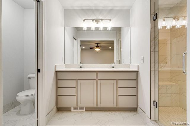 bathroom featuring ceiling fan, a shower with door, vanity, and toilet