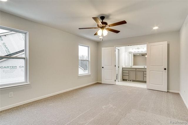 unfurnished bedroom featuring ceiling fan, light colored carpet, and ensuite bath