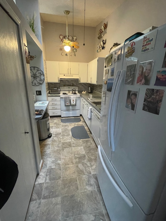 kitchen featuring white cabinetry, hanging light fixtures, a high ceiling, tasteful backsplash, and white appliances