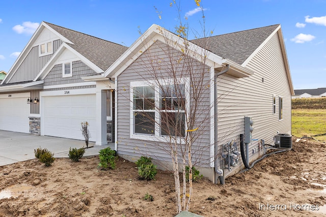 view of front of house featuring central air condition unit, a garage, driveway, and a shingled roof