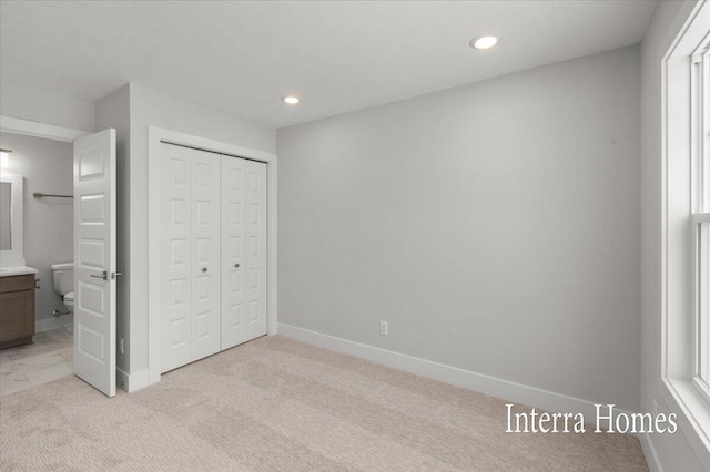 unfurnished bedroom with baseboards, light colored carpet, recessed lighting, ensuite bathroom, and a closet