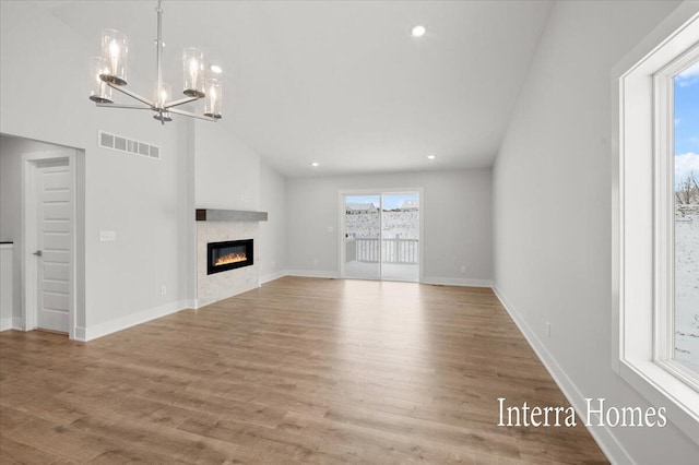 unfurnished living room featuring visible vents, baseboards, a chandelier, light wood-style flooring, and a glass covered fireplace