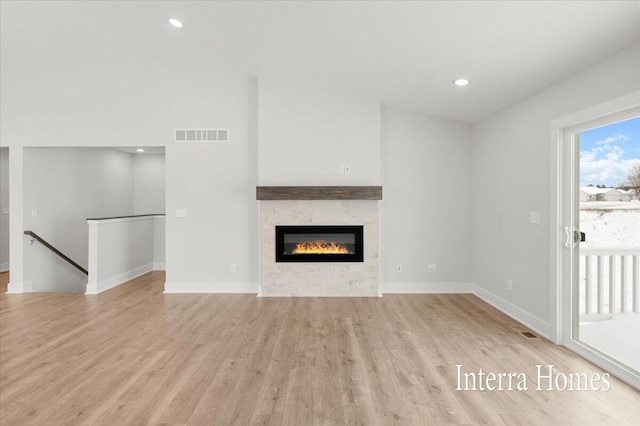 unfurnished living room featuring recessed lighting, light wood-type flooring, baseboards, and a glass covered fireplace