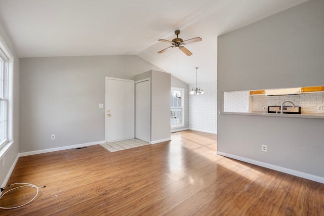 unfurnished living room with ceiling fan with notable chandelier, a healthy amount of sunlight, vaulted ceiling, and light hardwood / wood-style flooring