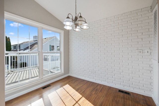 unfurnished dining area with vaulted ceiling, brick wall, a notable chandelier, and wood-type flooring