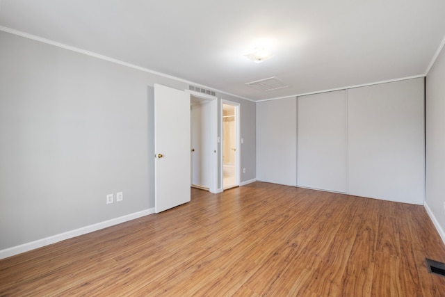 unfurnished bedroom with ensuite bath, a closet, light hardwood / wood-style flooring, and ornamental molding