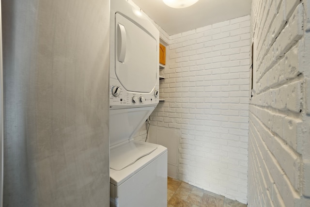 clothes washing area with brick wall and stacked washer and clothes dryer