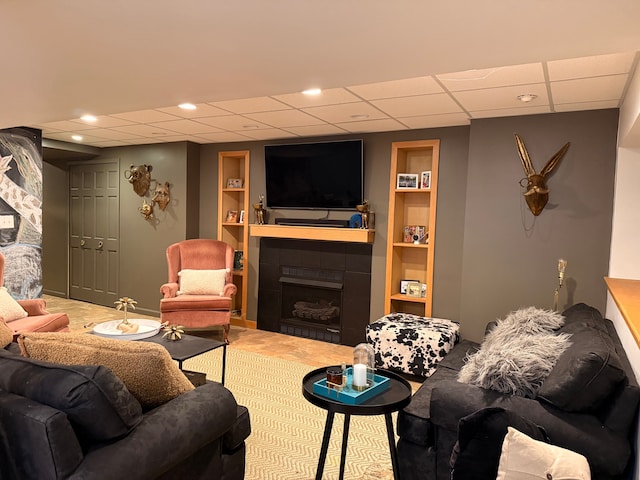 living room with a paneled ceiling, a fireplace, and built in shelves